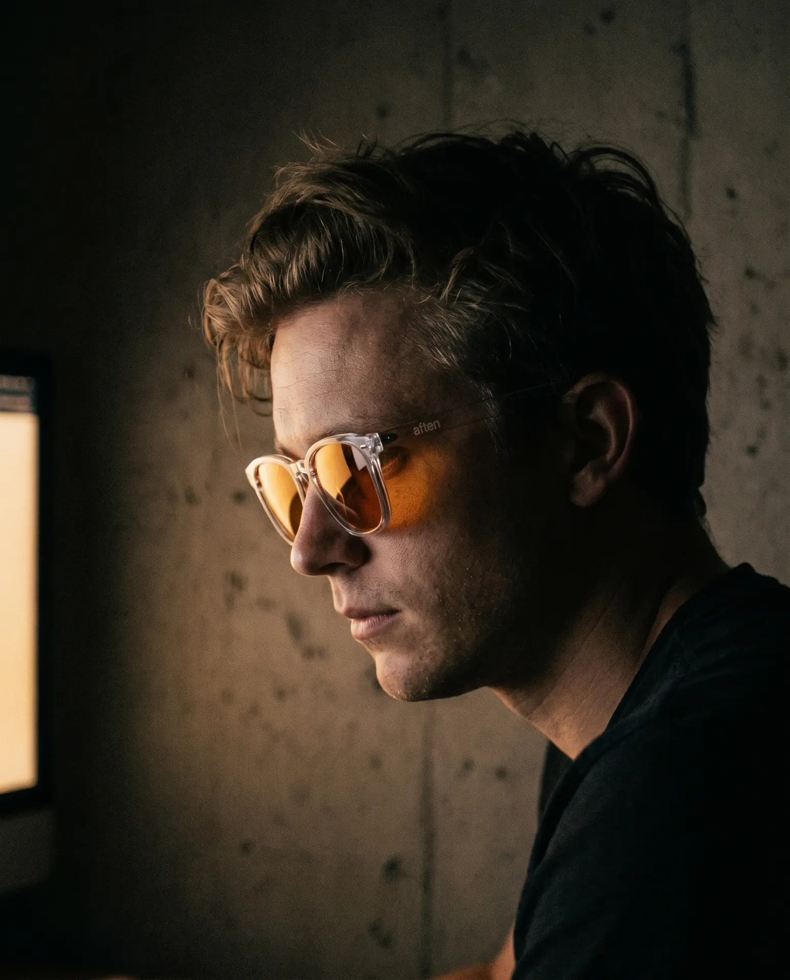 A man wearing AFTEN One glasses at a screen in a dark room