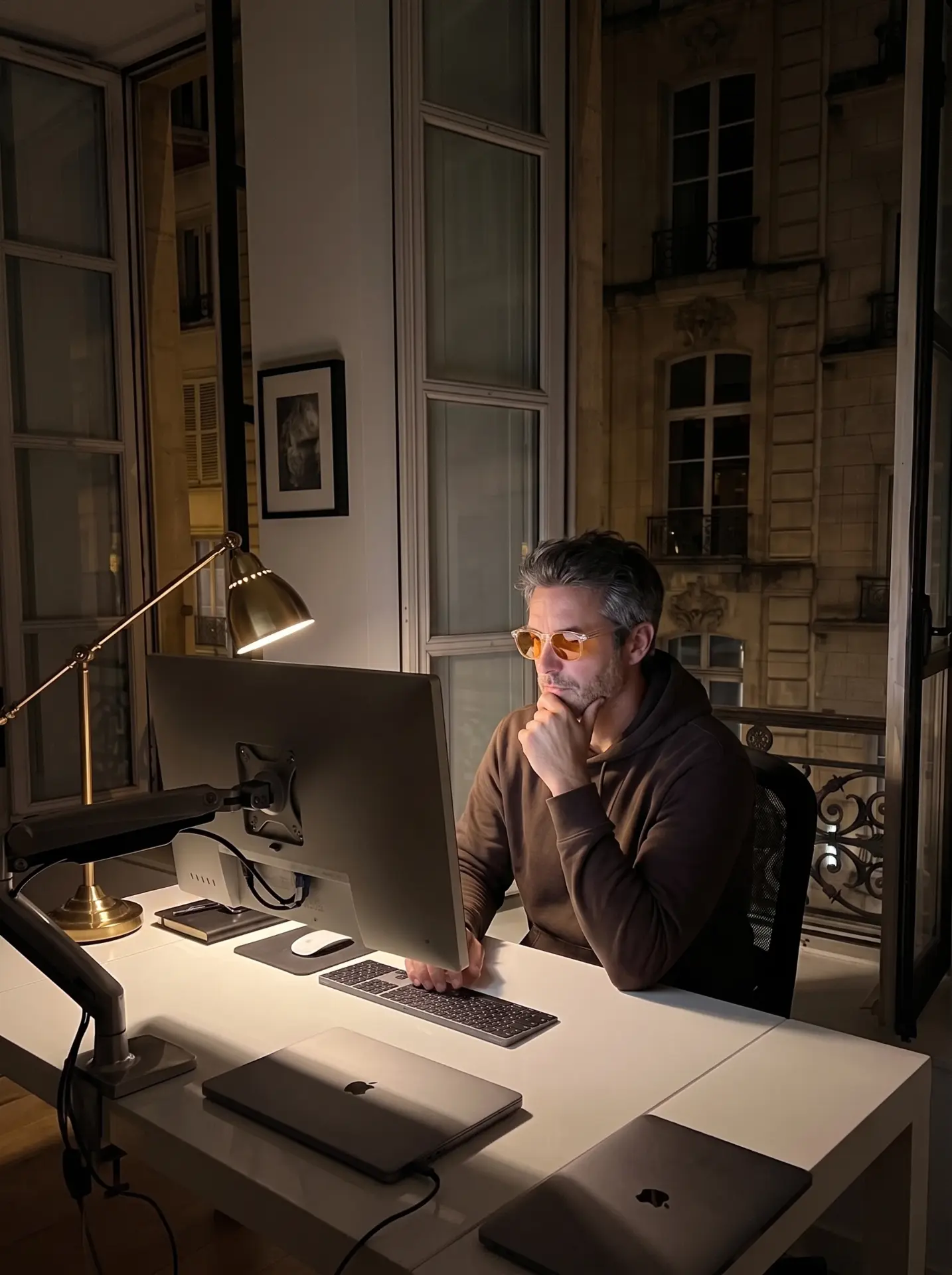 A man in amber glasses working at a monitor after dark